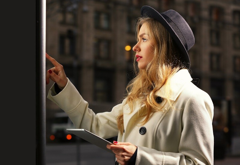 Young woman near digital screen in street at evening time